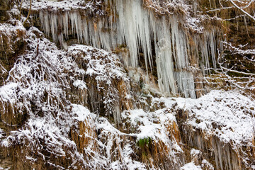 a rock in snow, icicles and dry grass