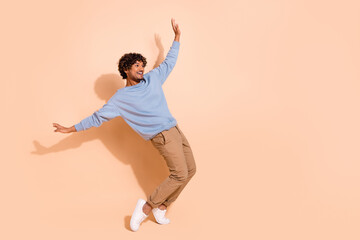 Full body photo of carefree guy wear blue shirt trousers stand on tiptoes look at sale empty space isolated on beige color background