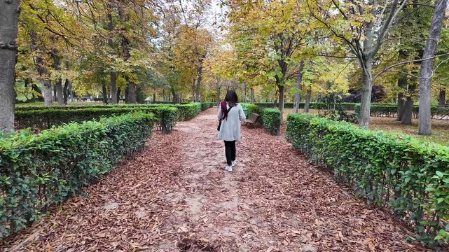 A woman strolling through the colorful autumn gardens of Retiro Park in Madrid, surrounded by nature.
