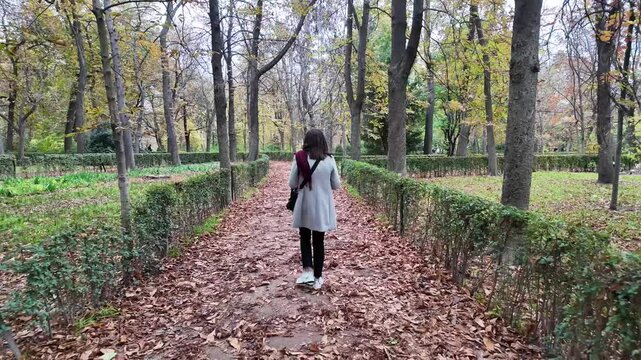 A woman strolling through the colorful autumn gardens of Retiro Park in Madrid, surrounded by nature.
