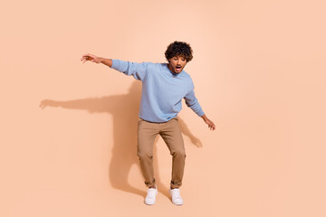 Full body photo of stunned guy wear blue shirt trousers standing on tiptoes look down at empty space isolated on beige color background © deagreez