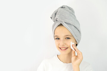 Beautiful teen girl with a towel on her head smiling and cleansing her face with a cotton pad. Teen Skin Care, Moisturizing