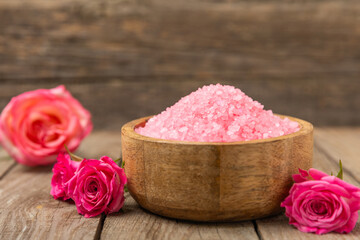 Sea salt for bath with aroma and rose flowers on textured wooden background. Pink sea salt. Spa treatments. Natural salt with herbs and essential oils. skincare concept. Meso for text. Copy space
