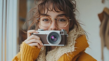 Young woman with brown hair and glasses holding vintage camera.