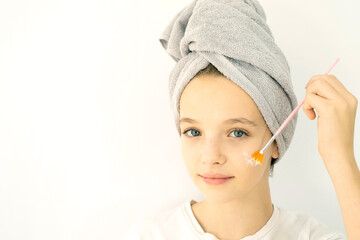 Beautiful teenage girl with towel on her head smiling and taking care of her facial skin with a brush. Skin care for a teenager. White background, space for text