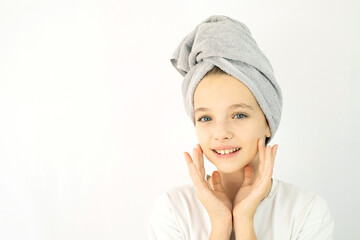 Beautiful teenage girl with towel on her head in white t-shirt on white background, smearing her face with cream. Teen Skin Care, Moisturizing