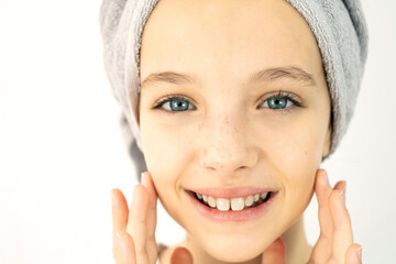 Beautiful teenage girl with towel on her head in white t-shirt on white background, smearing her face with cream. Teen Skin Care, Moisturizing