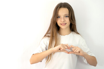 Heart love symbol. smiling woman with tilted head showing heart with her hands. White solid background. studio shot. Romantic mood. White t-shirt