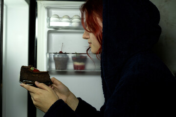 Woman in the kitchen having a late night snack, she is taking a delicious dessert from the fridge, diet fail concept
