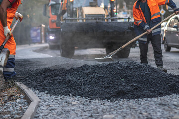 Road construction worker leveling asphalt with a shovel. Focus on foreground