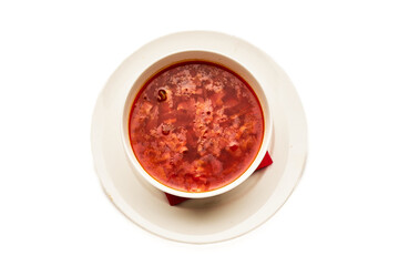 A bowl of red soup sits on a white plate with a red napkin underneath