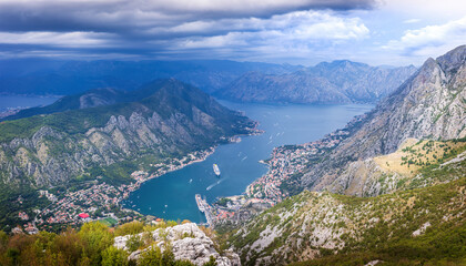 View of the Bay of Kotor, Montenegro, from a high mountain road with winding switchbacks. The scenic panorama includes the towns of Kotor and Tivat, and the Adriatic Sea.