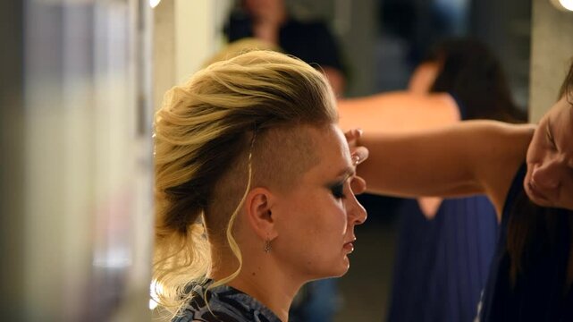 Close-up view of make-up artist applying eyeshadow using finger on eyes of adult blond haired woman with mohawk hairstyle in beauty salon. Soft focus. Real time handheld video. Beauty industry theme.