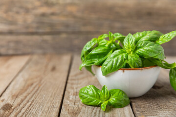 Green basil leaves on a textured wooden background. Kitchen herbs, spices. Fresh green organic basil. Vegan. Greens for salad. Place for text. Copy space.