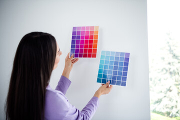 Woman selecting color palettes indoors, wearing casual pullover during daylight, showcasing...