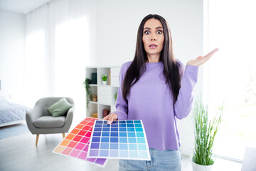 Charming brunette woman puzzled with color palettes in bright living room interior
