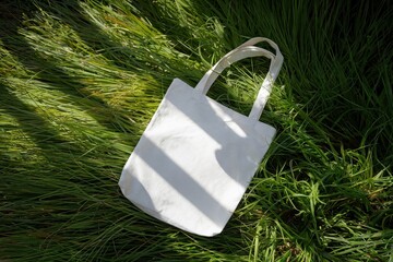 Blank white tote bag on lush green grass under dappled sunlight with soft shadows and crinkled fabric adding texture and depth to the vibrant scene