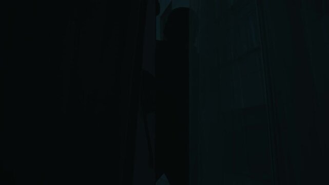 Tilt up view of unrecognisable thief in black clothes with crowbar breaking into apartment through window at night