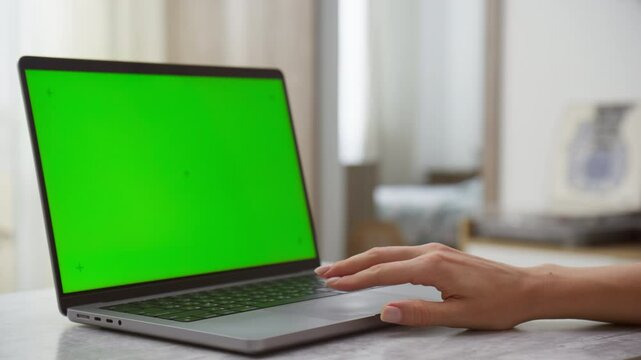 Close-up of female hand using touchpad on laptop with green screen