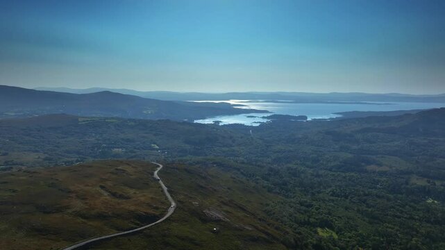 Caha Pass, County Cork, Ireland, September 2024. Drone pulls backwards north west above winding scenic road with Glengarriff and the North Atlantic Ocean in the distance.