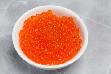 Red salmon caviar in a white bowl on the kitchen table.