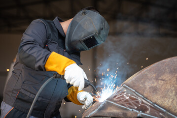 Welder joining metal parts with sparks flying around in workshop