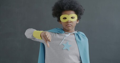 Portrait of unhappy African American boy showing thumbs-down hand gesture expressing disappointment on grey background. Childhood and negative emotion concept. - Powered by Adobe