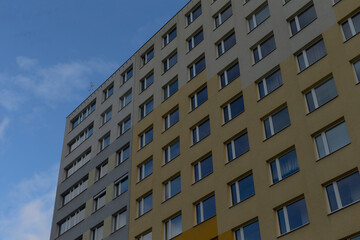 A contemporary apartment block featuring large windows set against a bright blue sky above it