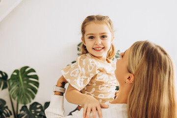 Smiling, happy, beautiful woman, mother holding little daughter, standing in living room at home