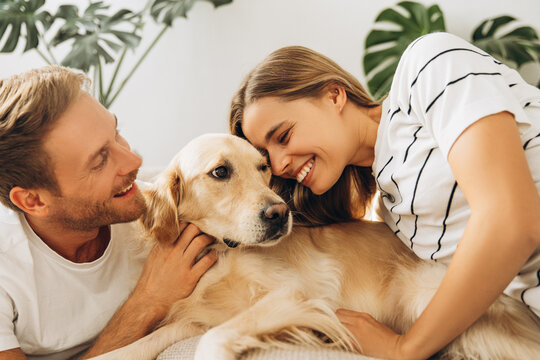 Portrait of smiling young couple, attractive man and woman hugging golden retriever - Powered by Adobe