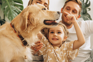 Happy, beautiful mother, father, cute little daughter playing together with dog, golden retriever