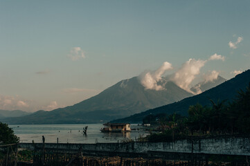 Tranquil morning at Lake Atitlan featuring a boat and a lakeside cabin surrounded by mountains in...