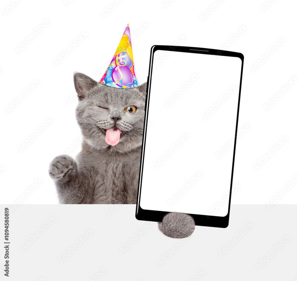 Aufkleber Winking kitten with tongue out wearing party cap shows big smartphone with blank screen above empty white banner. Empty space for text. isolated on white background