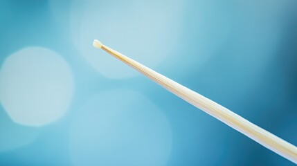 Close-up of a single toothpick with a smooth tip against a soft blue background featuring a delicate bokeh effect for added depth.