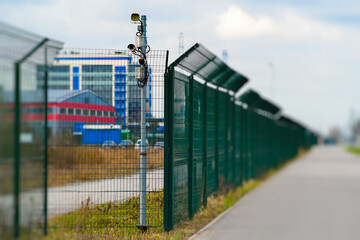 A security fence equipped with advanced surveillance equipment located near an industrial area