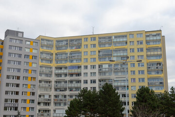 A multistory apartment building with vibrant yellow accents is surrounded by lush green shrubbery