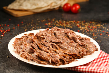Portion Doner kebab meat served in plate with Pita Bread, knife, fork and tomato isolated on wooden background closeup side view of arabic and turkish fast food