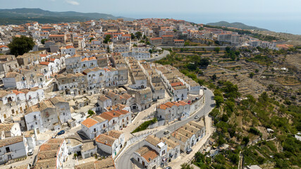 Aerial view of houses and buildings in the historic center of Monte Sant'Angelo, in the province of Foggia, Apulia. It is a typical village of Southern Italy. In background is the Mediterranean Sea.