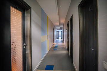  Modern hallway with gray floors, colorful wall accents, closed doors, and natural light streaming from the glass door at the end.