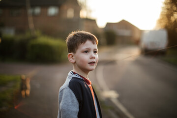 Young boy outdoors on suburban street in warm evening sunlight shallow depth of field natural...