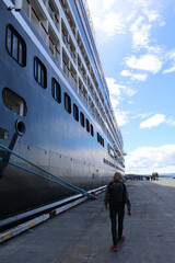 solo man walking alongside the hull of a tall cruise ship that is docked