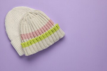 Warm woolen hats on lilac background, top view. Space for text