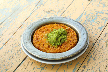 Arabic Kunafa or Baklava topped with chopped pistachio served in plate isolated on wooden table side view of arabic and turkish dessert