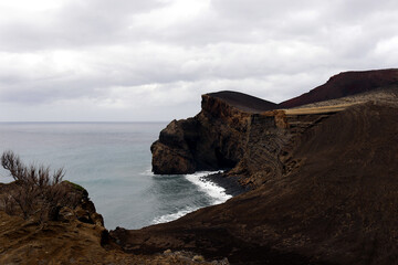 Saint Helena's Isolated and volcanic coastline: Dark sands and smooth boulders stretch along a mist-shrouded shoreline, framed by steep cliffs and the endless expanse of the Atlantic Ocean.