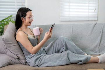 Young woman relaxing on sofa using smartphone and drinking coffee