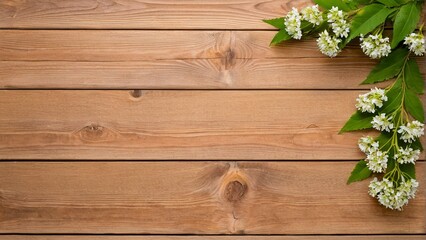 A wooden surface with a branch of white flowers and green leaves on the right side.