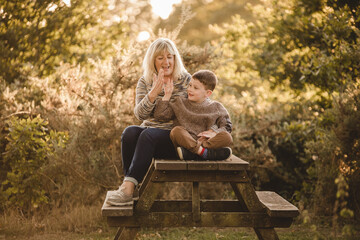 Grandmother and young boy clapping hands and smiling on a wooden bench, fall setting