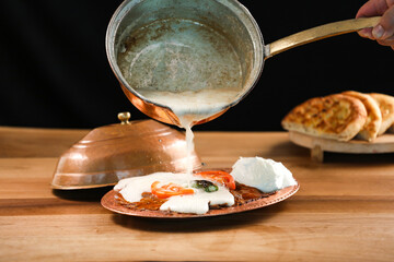 Turkish Meat Iskender Kebab topped with creamy sauce yogurt, tomato and green chilli served in golden sizzling plate with pita bread isolated on wooden table side view of turkish food