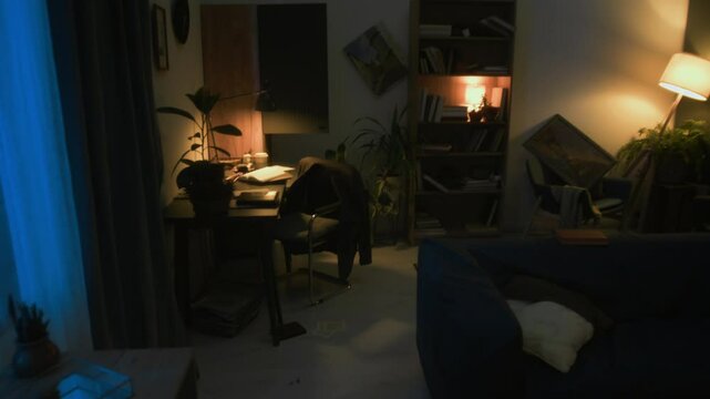 No people tilt down view of lamp-lit messy living room with open door of closet, fallen pictures and pulled out dresser drawer after robbery