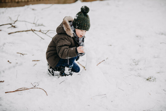 Child playing in snow crouching outdoors in winter clothing